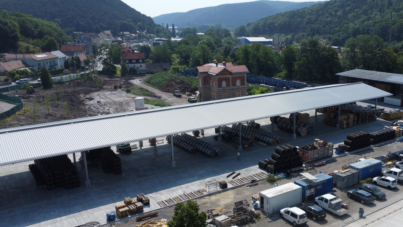 Neues Lagergebäude unter einem großen Flugdach mit Lagerrollen und Materialien auf einer offenen Fläche.