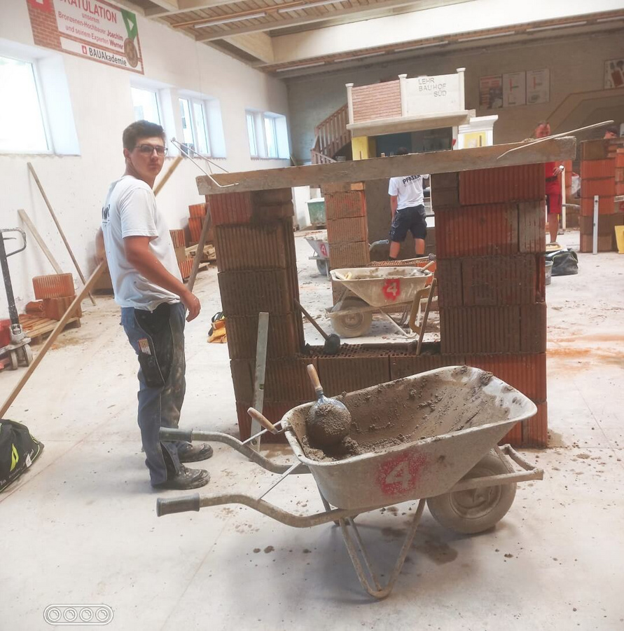 Ein Pfnier-Lehrling steht vor einer halbfertigen Mauer in der Bauakademie Übelbach und bereitet sich auf seine Abschlussprüfung vor.