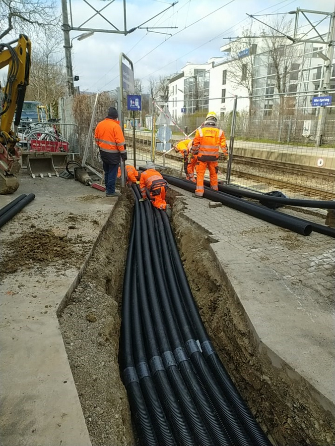 Bauarbeiter von Pfnier & Co GmbH verlegen Rohre in einem Graben nahe den Bahngleisen an einer Kreuzung in Wien, um die Sicherheit der Bahnstrecken zu verbessern.