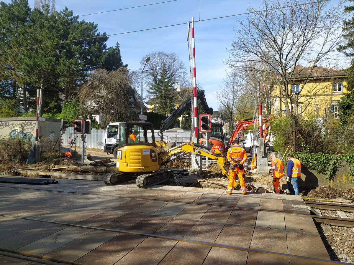 Bauarbeiter von Pfnier & Co GmbH bei der Errichtung provisorischer Rohrtrassen an einer Bahnkreuzung in Wien, mit Bagger und Baumaschinen im Einsatz.