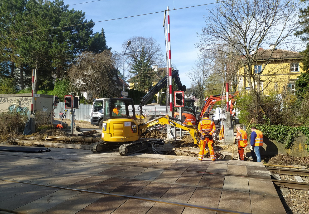 Bauarbeiter von Pfnier & Co GmbH bei der Errichtung provisorischer Rohrtrassen an einer Bahnkreuzung in Wien, mit Bagger und Baumaschinen im Einsatz.