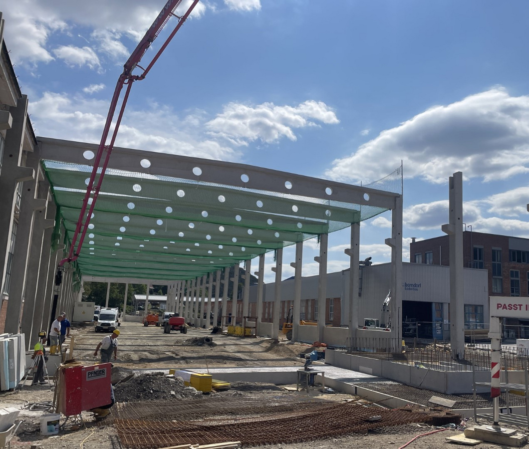 Arbeiter auf einer Baustelle unter einem großen Dachrahmen mit Sicherheitsnetzen, ein Teil des Berndorf-Projekts.