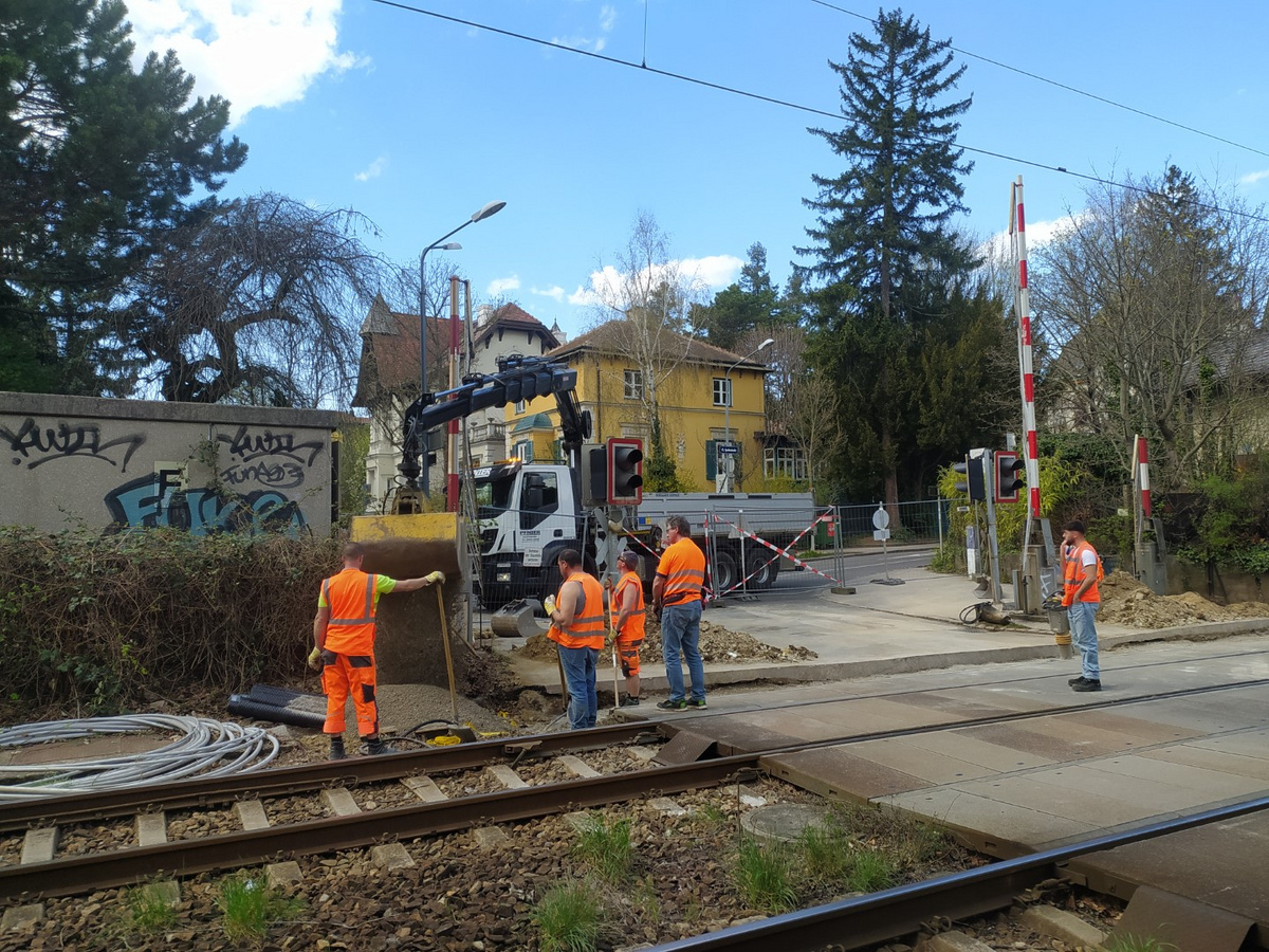 Pfnier-Bauarbeiter überwachen die Verladung von Baumaterialien an einer Bahnübergangsstelle in Wien, während ein LKW Baumaterial transportiert.